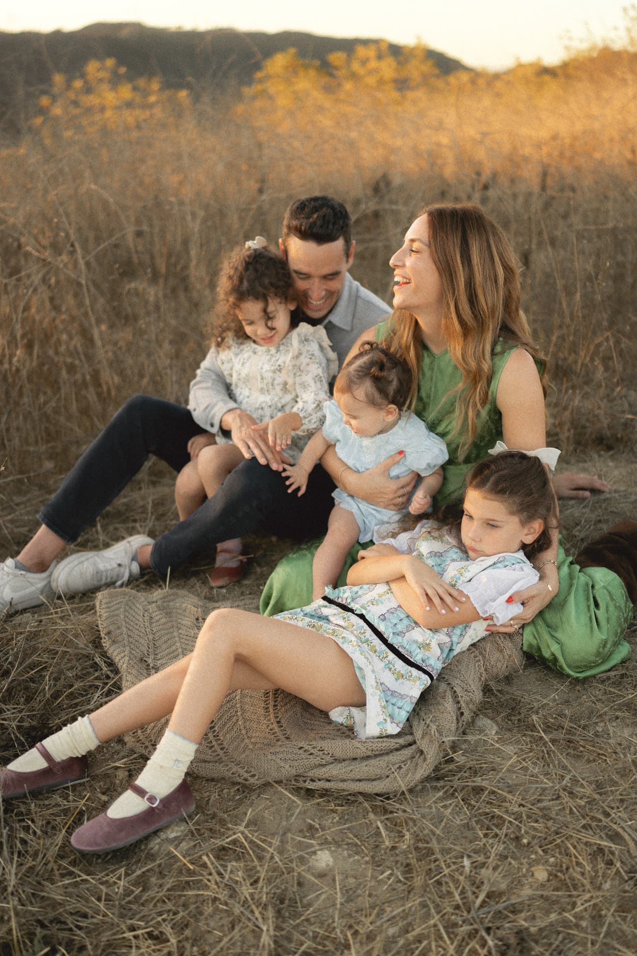 Family of five sitting together in a golden field at sunset