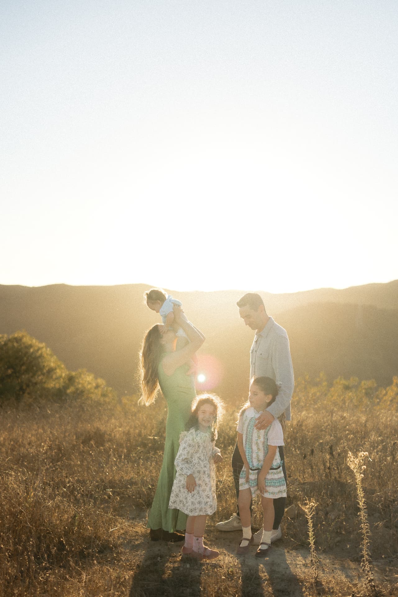 Family standing in a sunlit field as the sun sets behind the hills